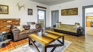 A living room with a brick fireplace, two sofas, a coffee table, and various wall decorations including a deer skull and a welcome sign. - Wine, Dine & Unwind: Hermann Home w/ Spacious Yard (Hermann)
