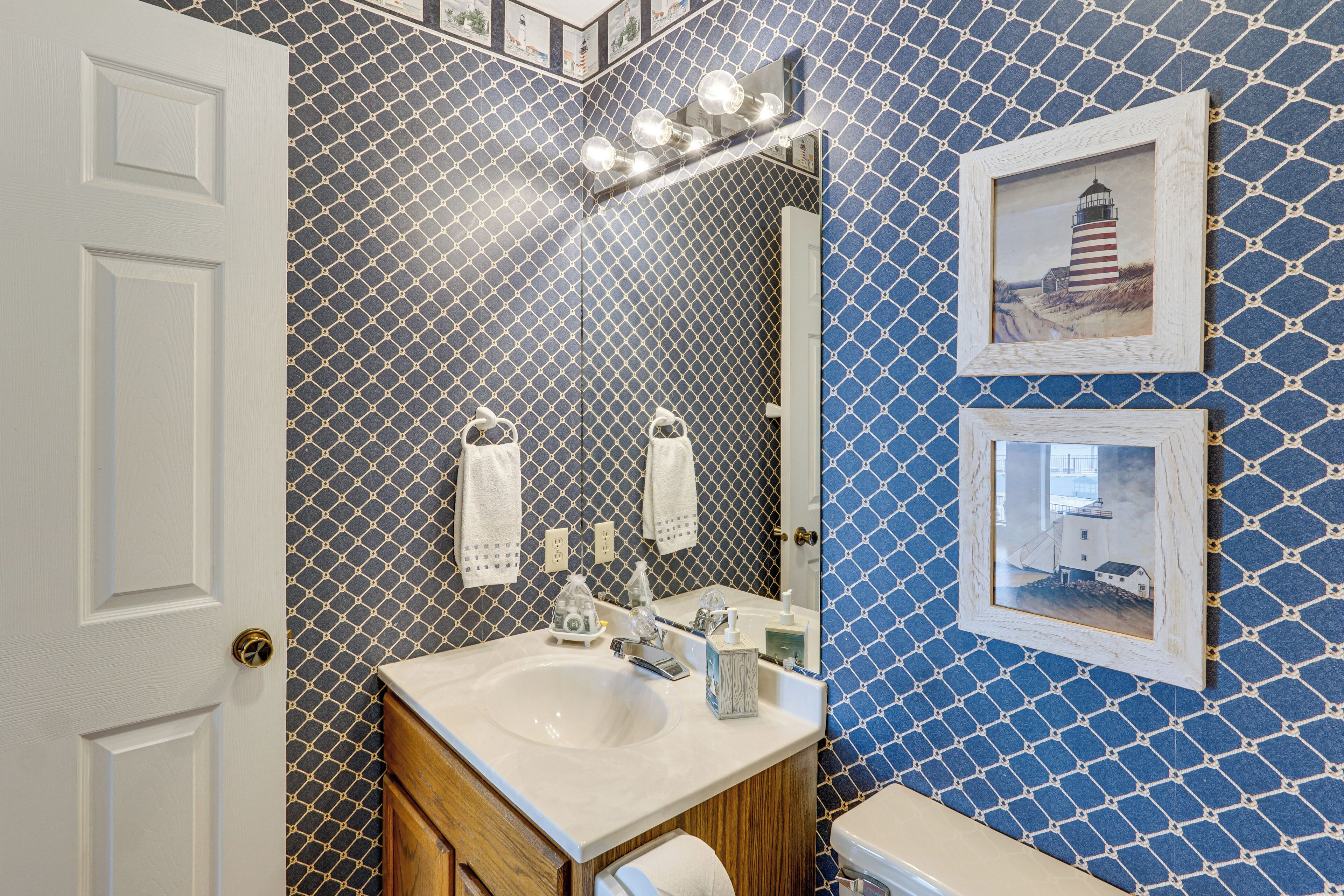 A bathroom with a white sink, wooden vanity, and a large mirror. There are towels hanging on the wall and a framed picture of a lighthouse.
