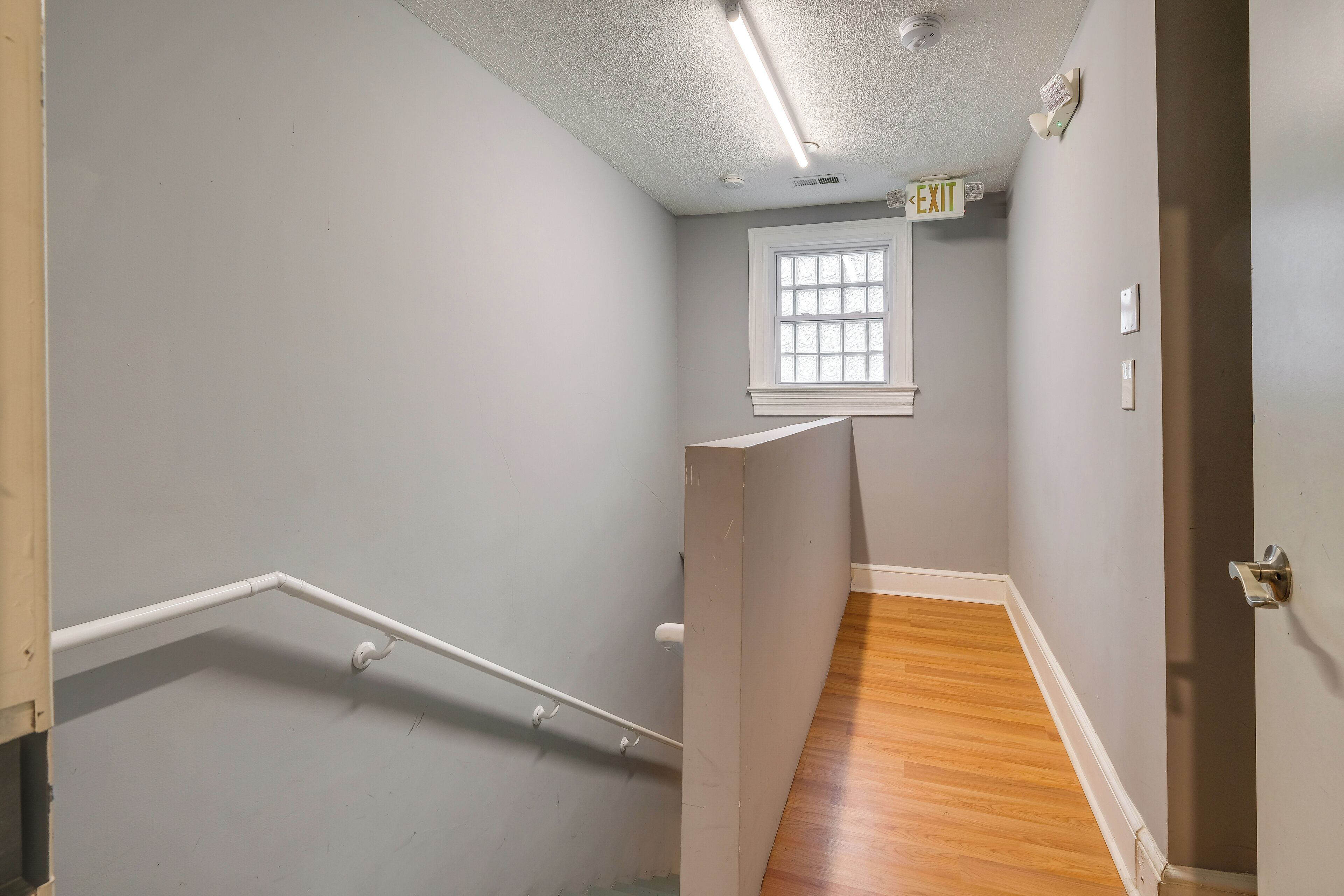 A staircase with a wooden finish and white handrails, leading to a landing with a window.