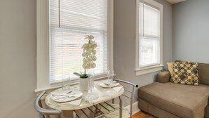A dining area with a table set for two, a potted orchid, and a sofa with patterned cushions. - Easy Metro Access: Wfh-friendly Apt 7 Mi to DC! (Silver Spring)