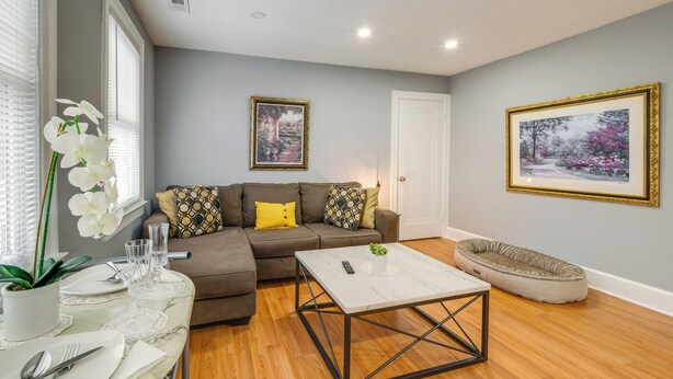 A living room with a sectional sofa, a coffee table, a pet bed, and two framed pictures on the wall. - Easy Metro Access: Wfh-friendly Apt 7 Mi to DC! (Silver Spring)