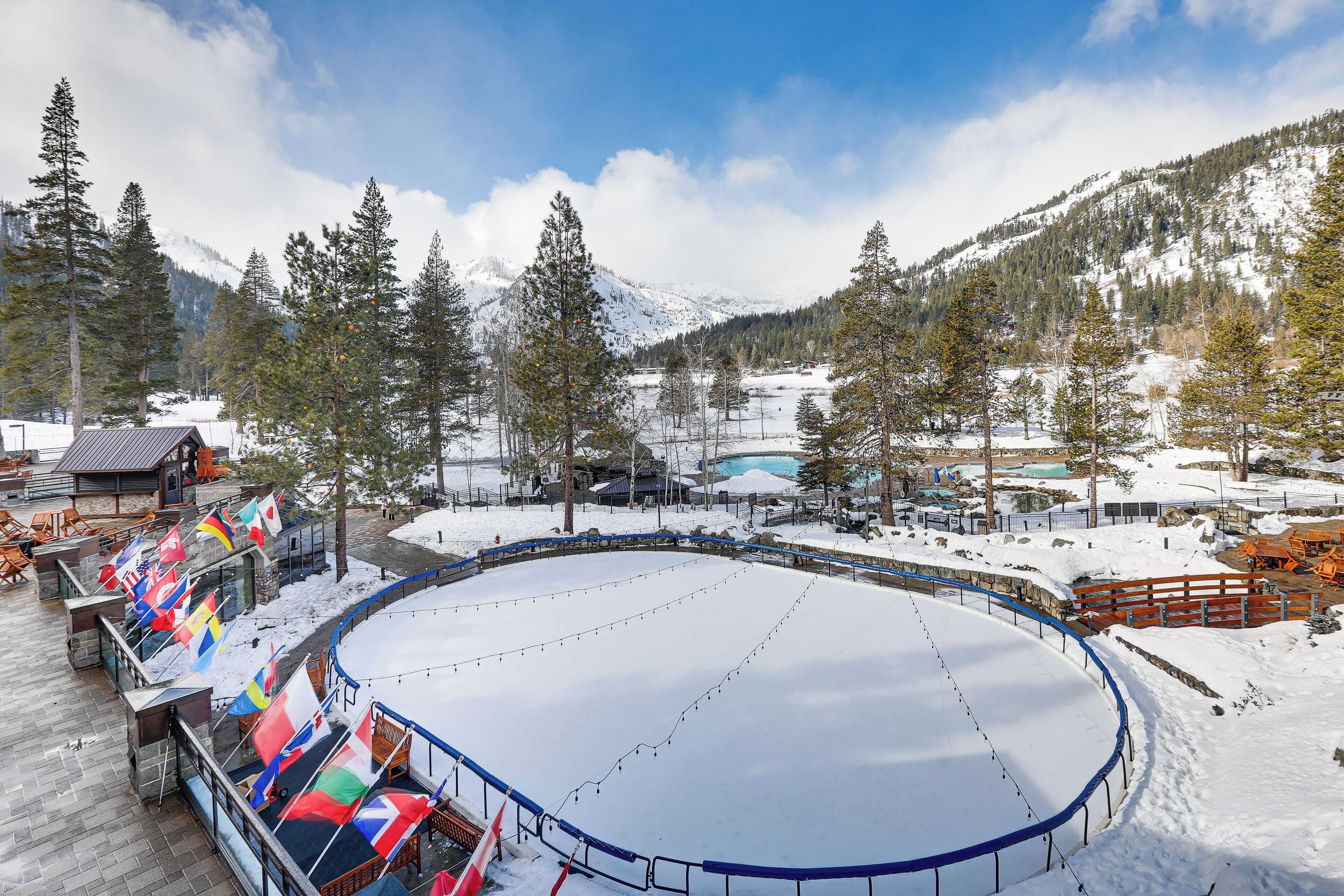 A snow-covered outdoor ice rink surrounded by mountains and trees.