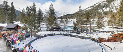 A snow-covered outdoor ice rink surrounded by mountains and trees.