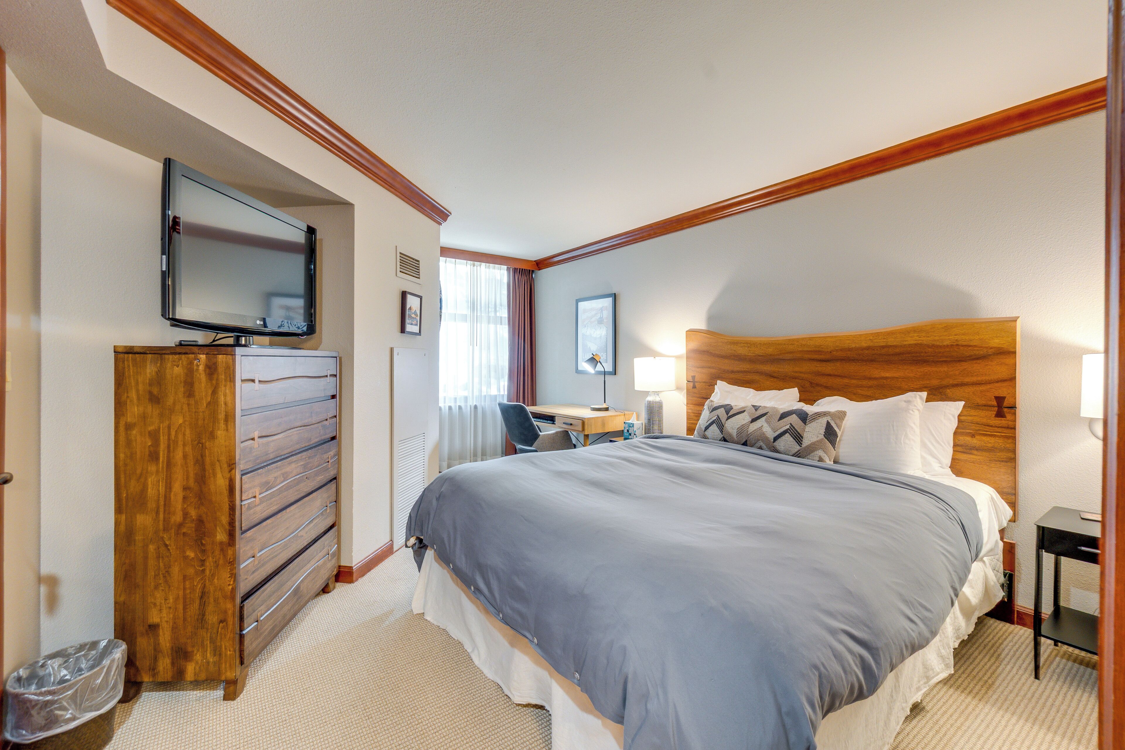 Ein Hotelzimmer mit einem großen Bett, einer Holzkommode, einem Schreibtisch und einem an der Wand befestigten Fernseher.