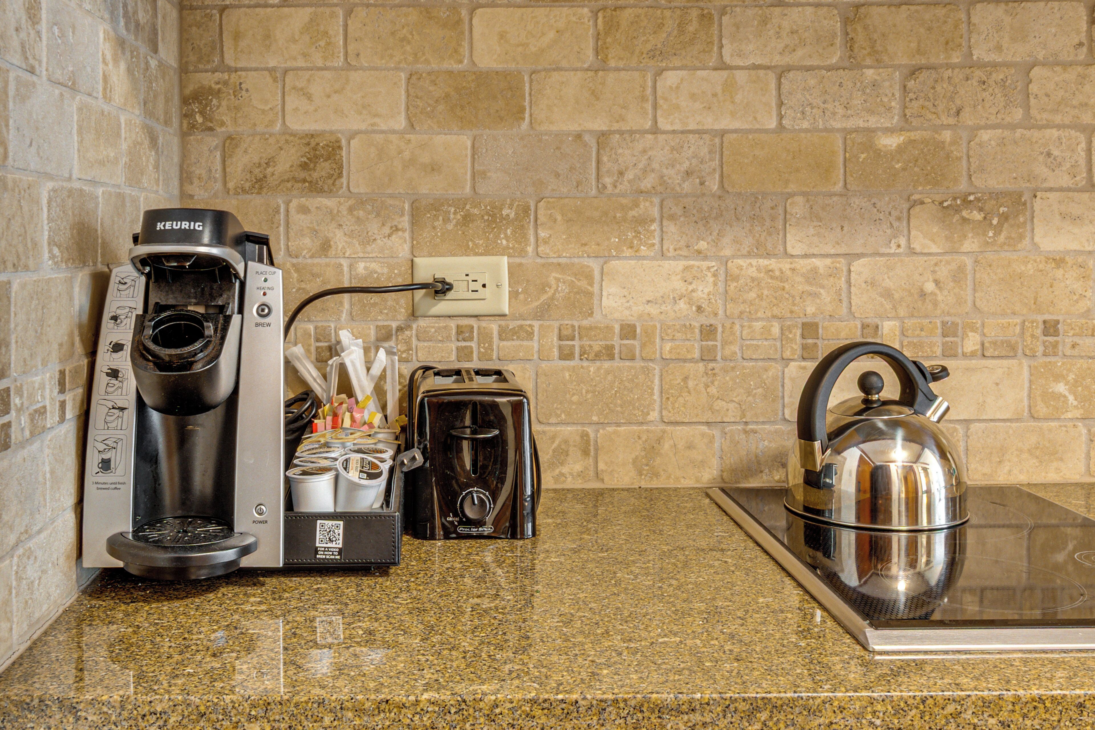 A kitchen with a coffee maker, toaster, kettle, and a granite countertop.