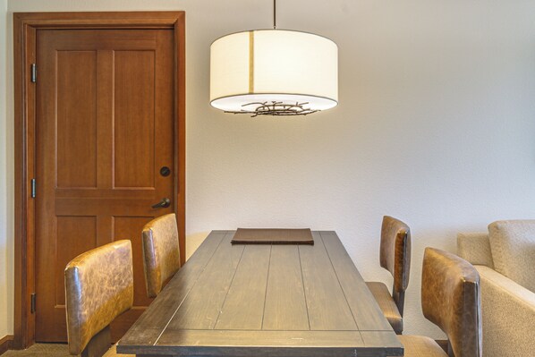 A dining area with a wooden table, chairs, a hanging lamp, and a wooden door.
