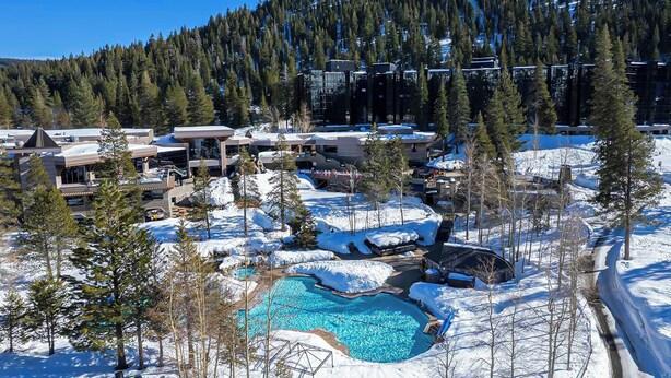 Un complexe hôtelier doté d’une piscine entourée de neige, de bâtiments et bordé par une montagne couverte de forêts.