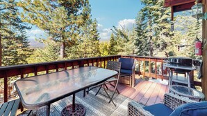 A wooden deck with a glass table and chairs, surrounded by tall trees and a mountain view. - 2BR Dog-friendly Cabin w/ Lake Views (Kings Beach)