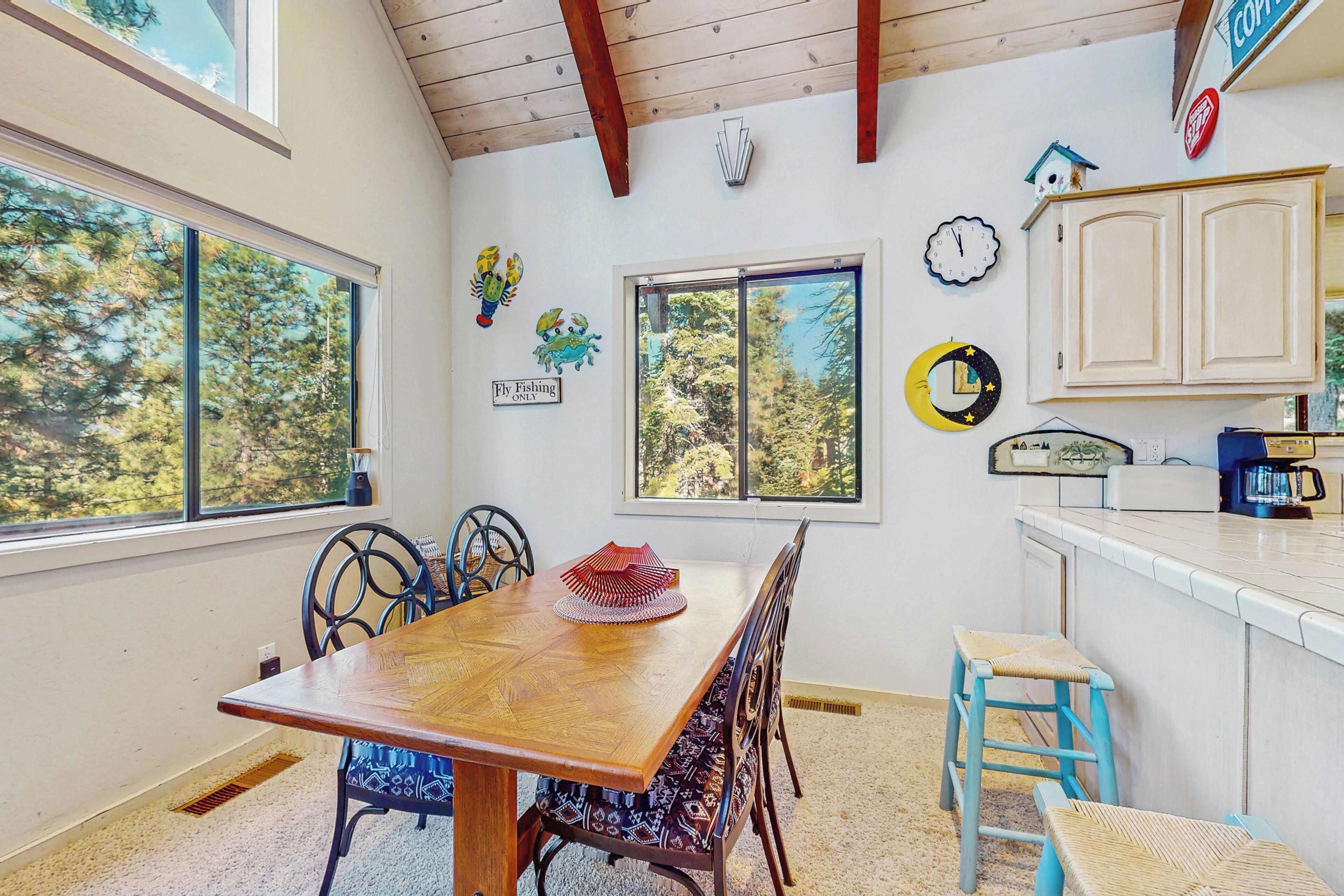 A dining area with a wooden table, chairs, and a view of trees through large windows.