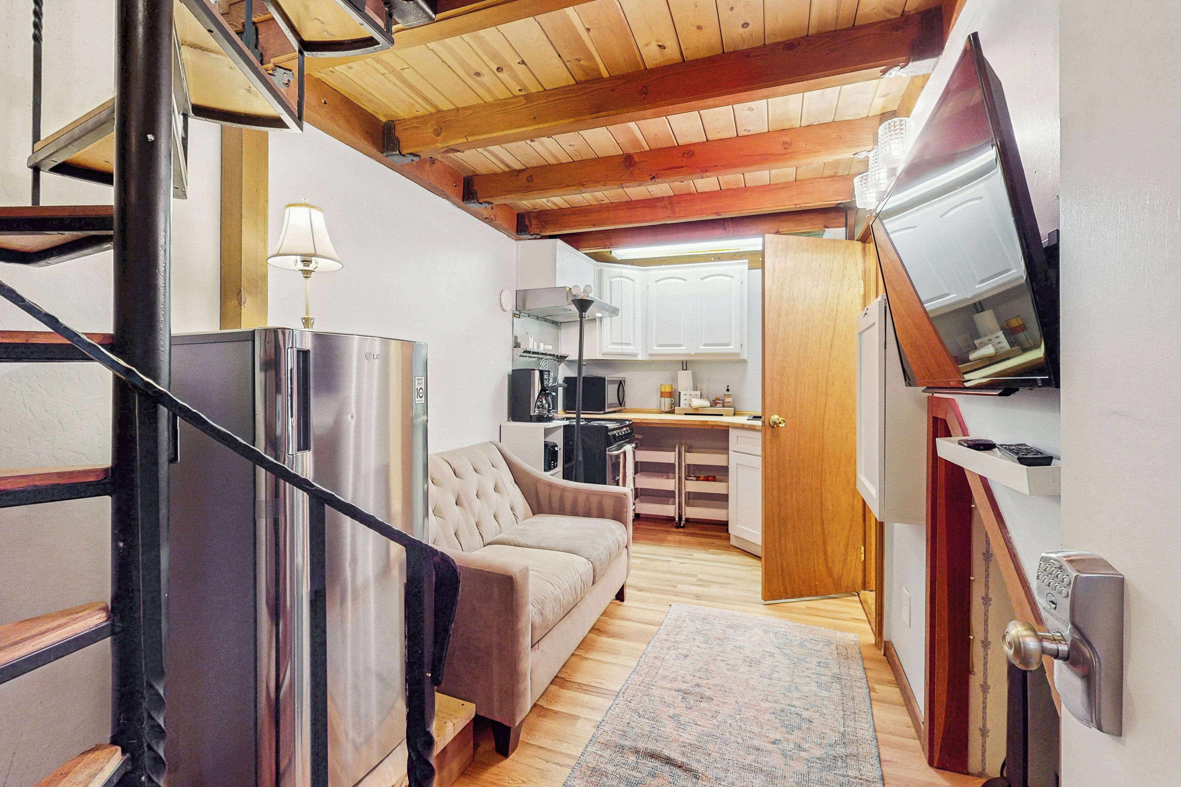 A compact living space with a kitchenette, a sofa, a lamp, and a television mounted on the wall.