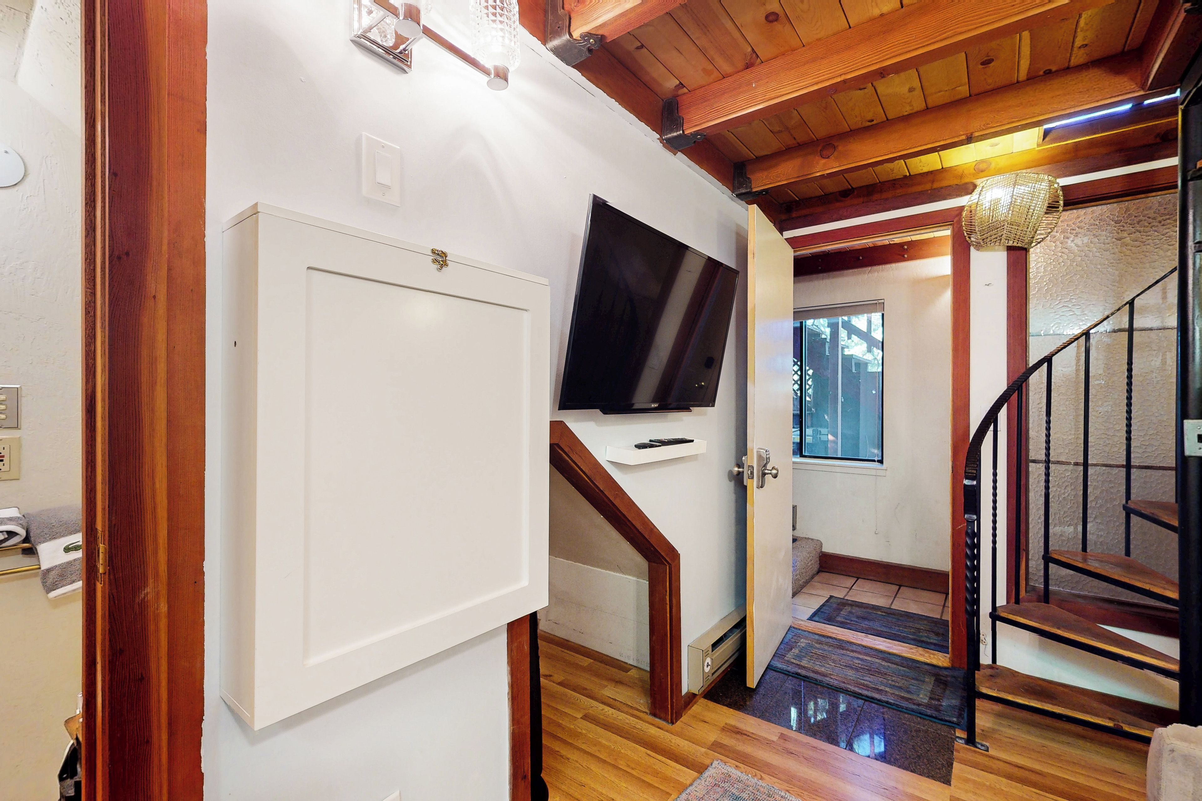 Una escalera de madera conduce a un segundo piso, donde hay un televisor montado en la pared.