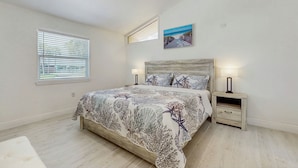 Une chambre à coucher avec un lit, une table de chevet, un ventilateur de plafond, une fenêtre avec des stores et un tableau au mur.