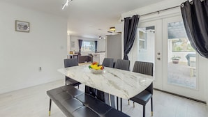 Un espace repas moderne avec une table en marbre, des chaises à revêtement noir et un centre de table composé d’un saladier rempli de fruits.