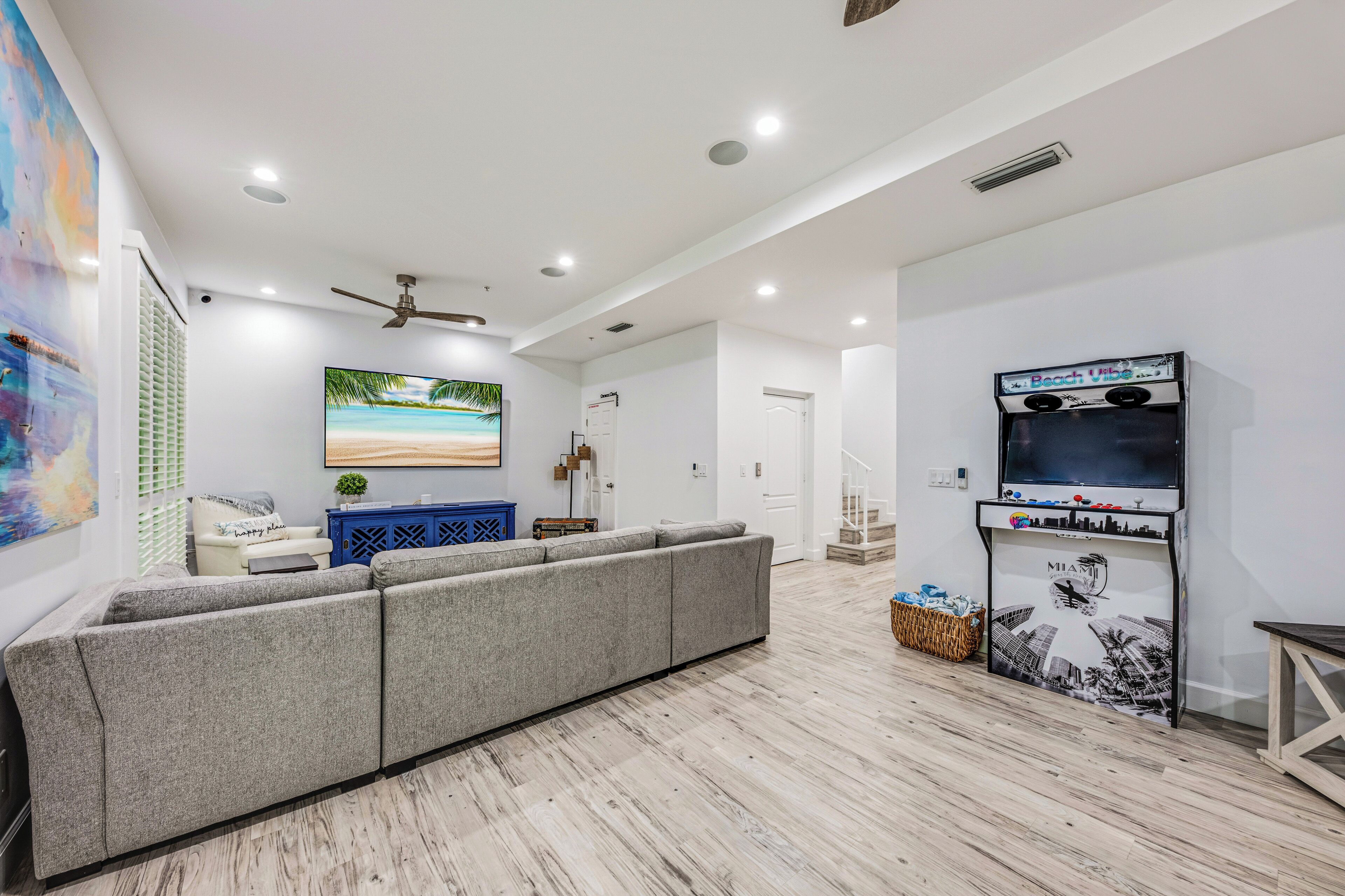 Una sala de estar moderna con un sofá seccional grisáceo, un televisor de pantalla plana y un cuadro con una escena de playa.