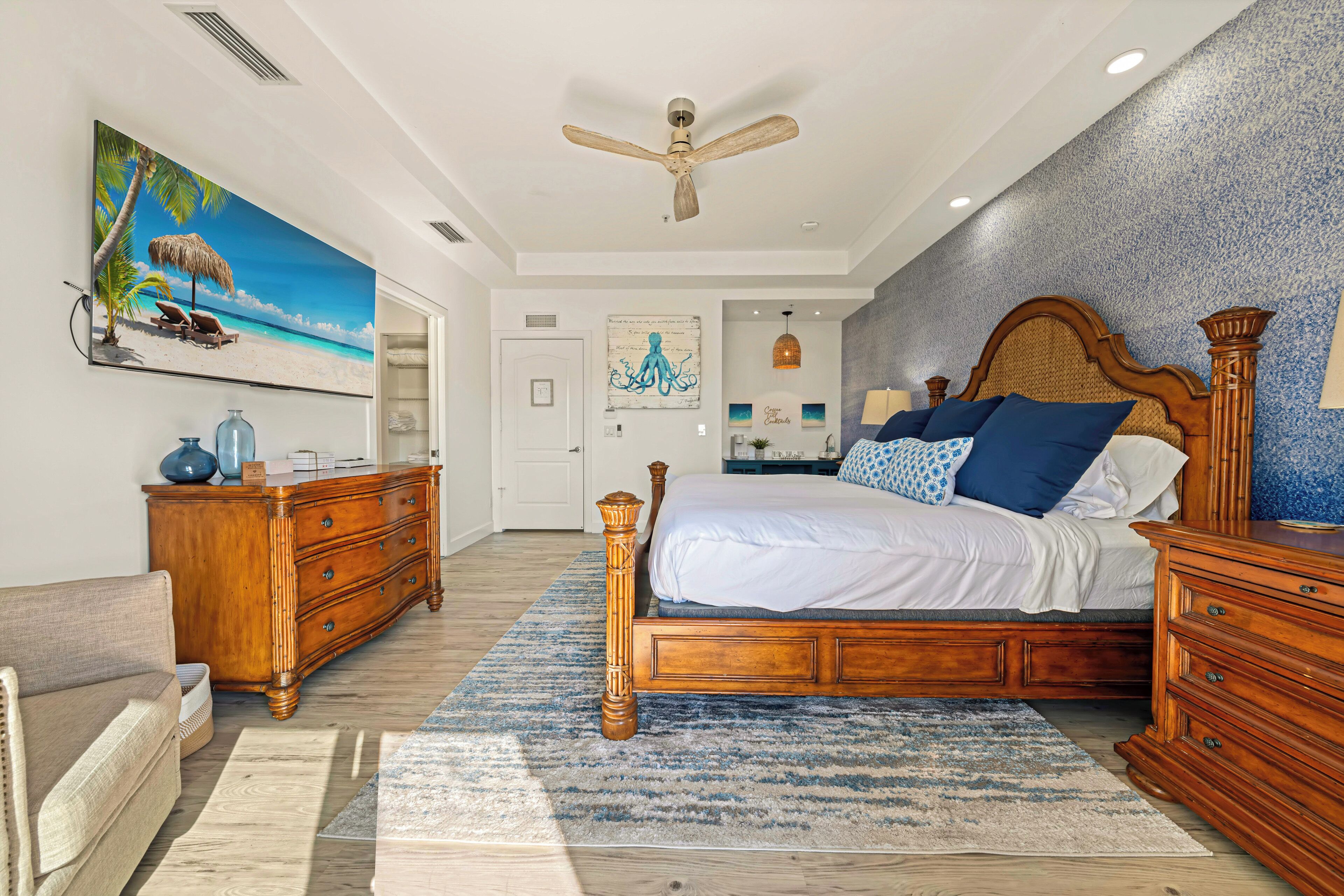 A bedroom with a wooden bed, a ceiling fan, a beach-themed painting, and a blue textured wall.