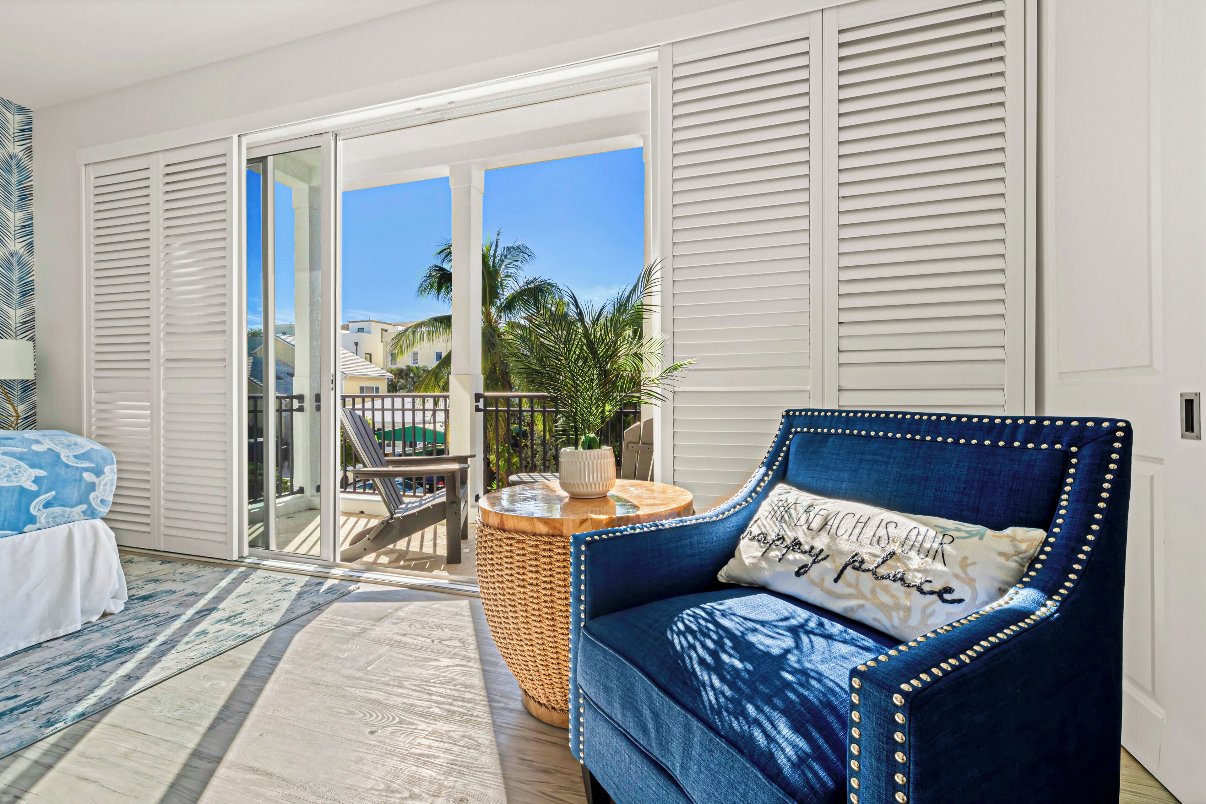 A bedroom with a bed, a blue sofa, a round wooden table, and a view of the outside balcony.