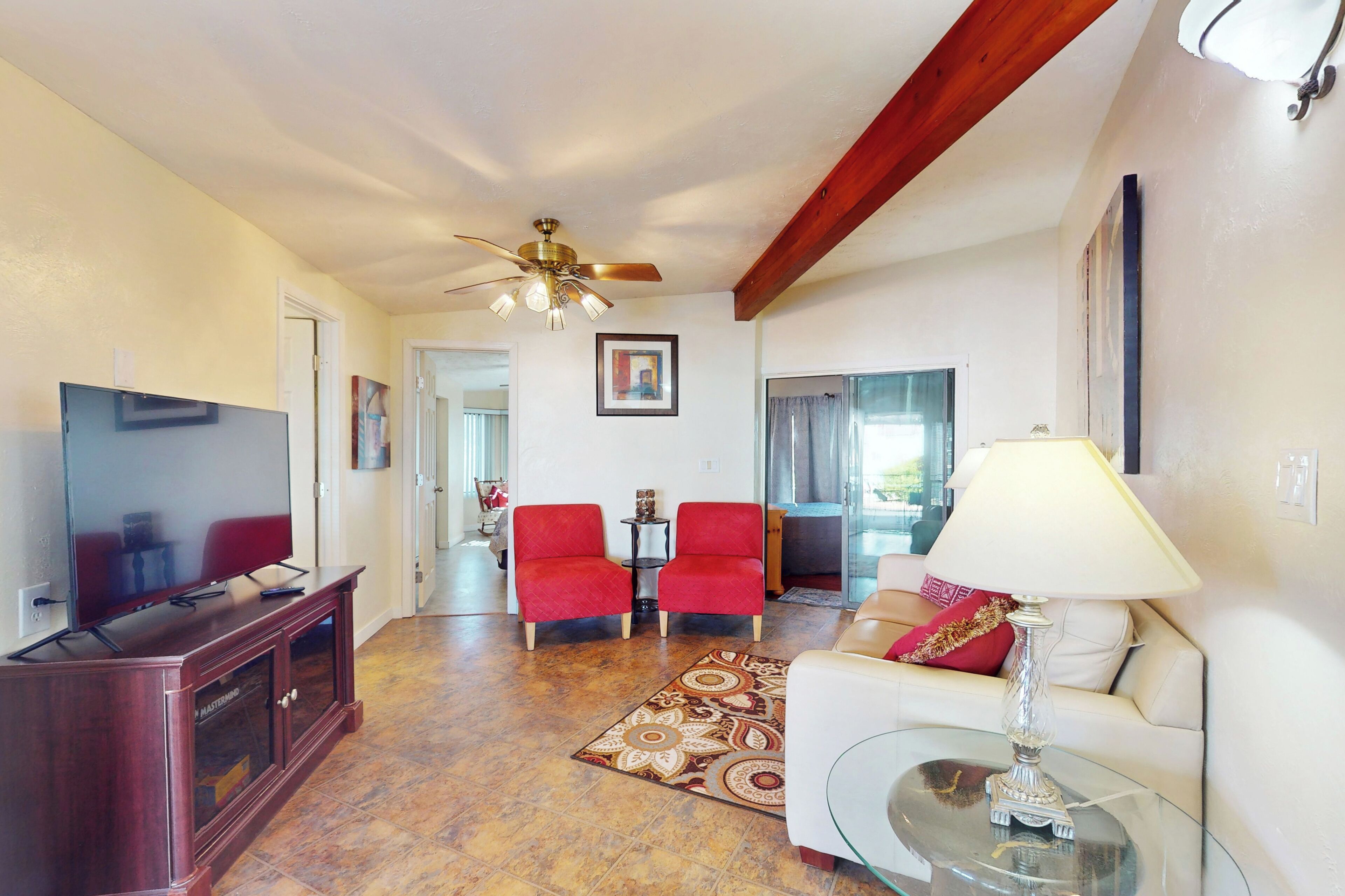 Un salon avec un téléviseur, des fauteuils rouges, une table basse en verre et un ventilateur de plafond.