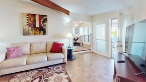 A spacious living room with a beige sofa, a patterned rug, a ceiling fan, and a large TV on a wooden stand. - Manufactured w/ Pools, Hot Tubs, Pickleball, AC (Surprise)