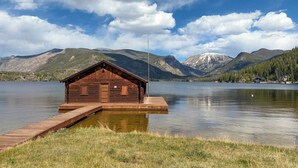 A wooden cabin on a dock by a lake with mountains in the background. - Granby Ranch Condo w/ Mtn-view: Trails & Hot-tub! (Granby)