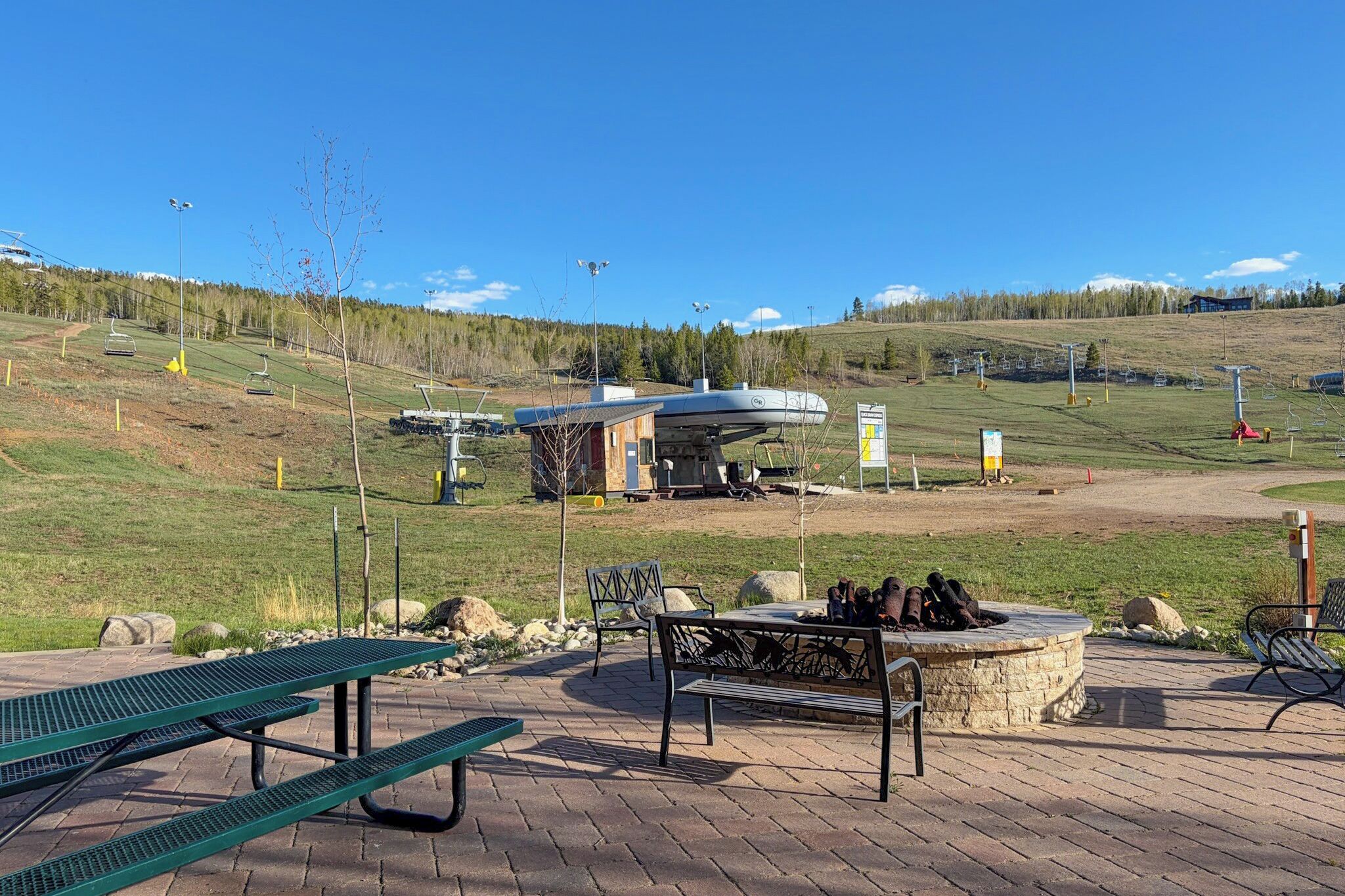 A park with picnic tables, a fire pit, and a ski lift in the background.