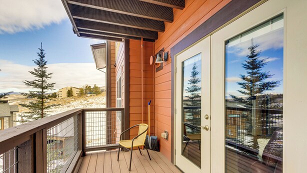 A balcony with a wooden floor, a chair, and a glass door with a view of trees and buildings. - Granby Ranch Condo w/ Mtn-view: Trails & Hot-tub! (Granby)