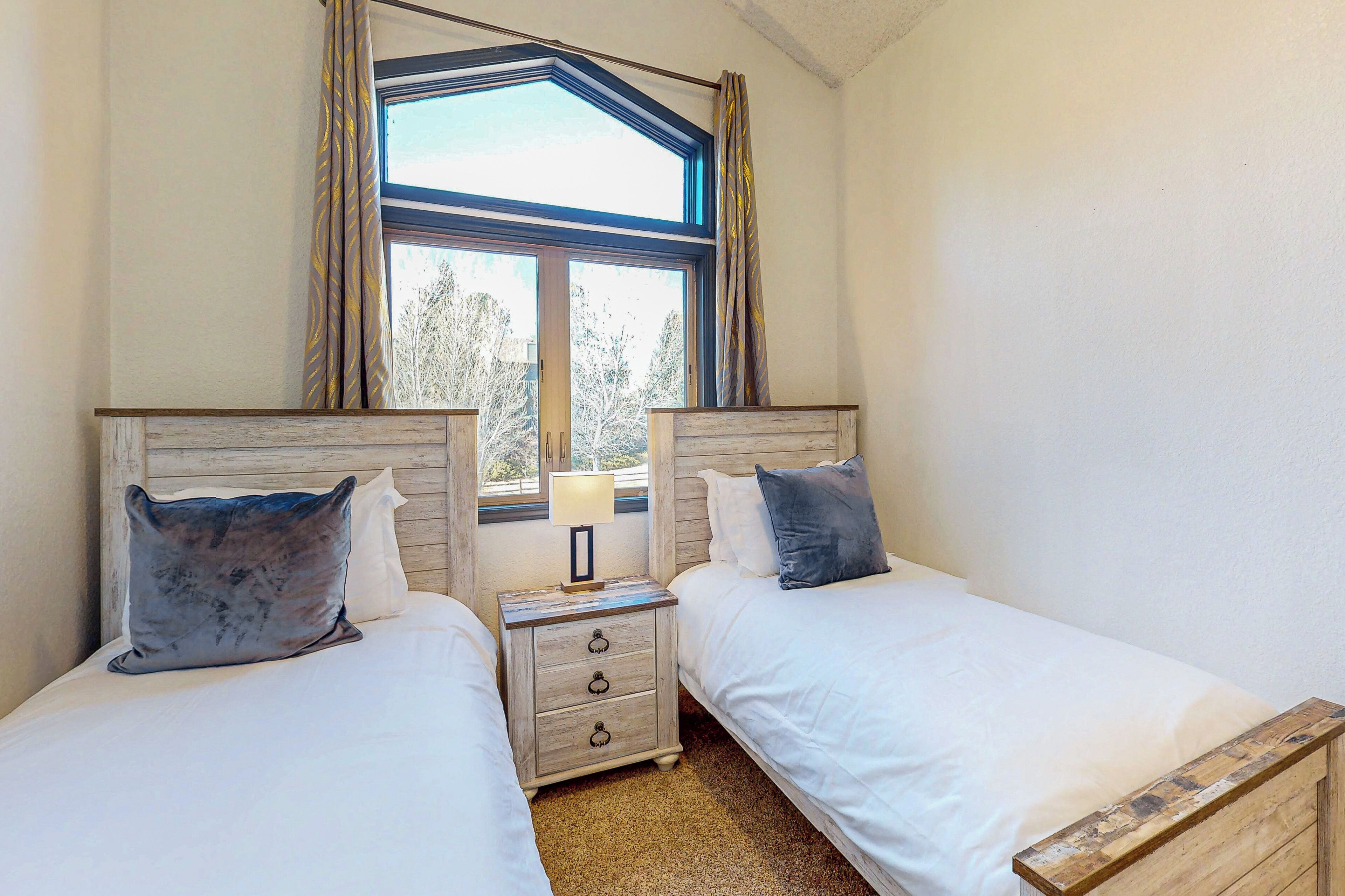 A bedroom with two beds, a nightstand with a lamp, and a window with curtains.