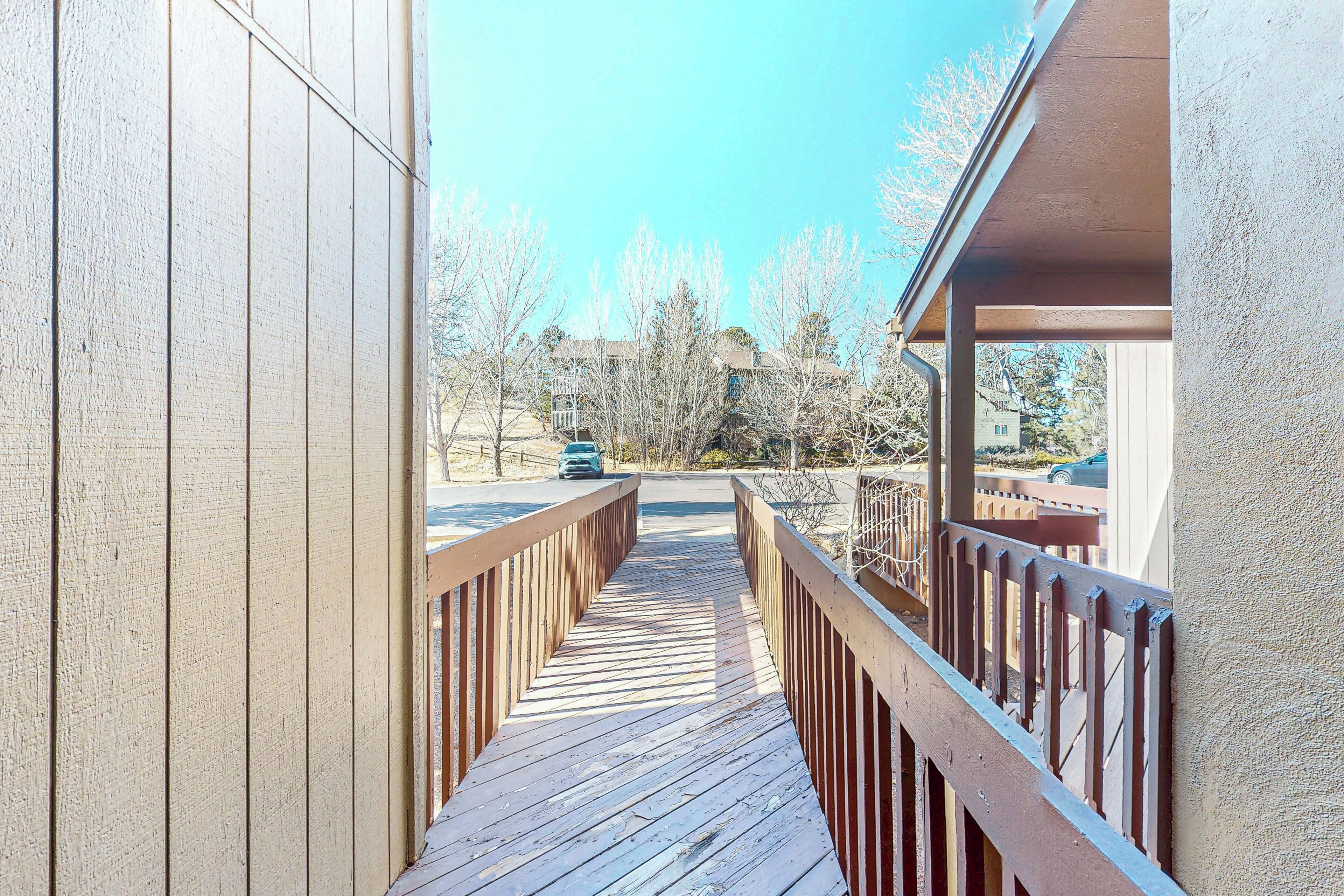 A wooden deck leading to a covered area with a view of a street and trees.