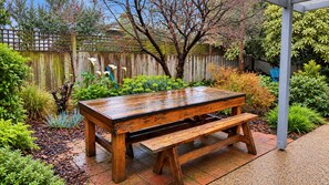 A wooden bench and table set in a garden with a wooden fence and various plants. - Aldebaran Road Beach House - perfect family coastal getaway, your search ends here (Ocean Grove)