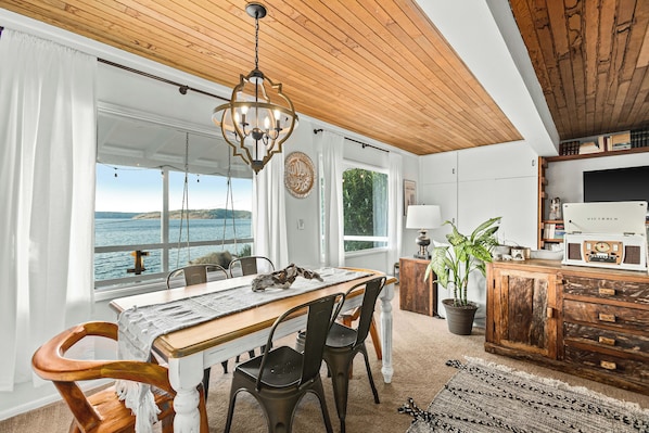 Un comedor con mesa de madera, sillas y vista al mar.