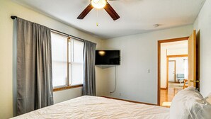 A bedroom with a bed, a ceiling fan, a TV mounted on the wall, and a door leading to another room. - Pet-friendly Home 2 Mi to Downtown Des Moines! (Des Moines)