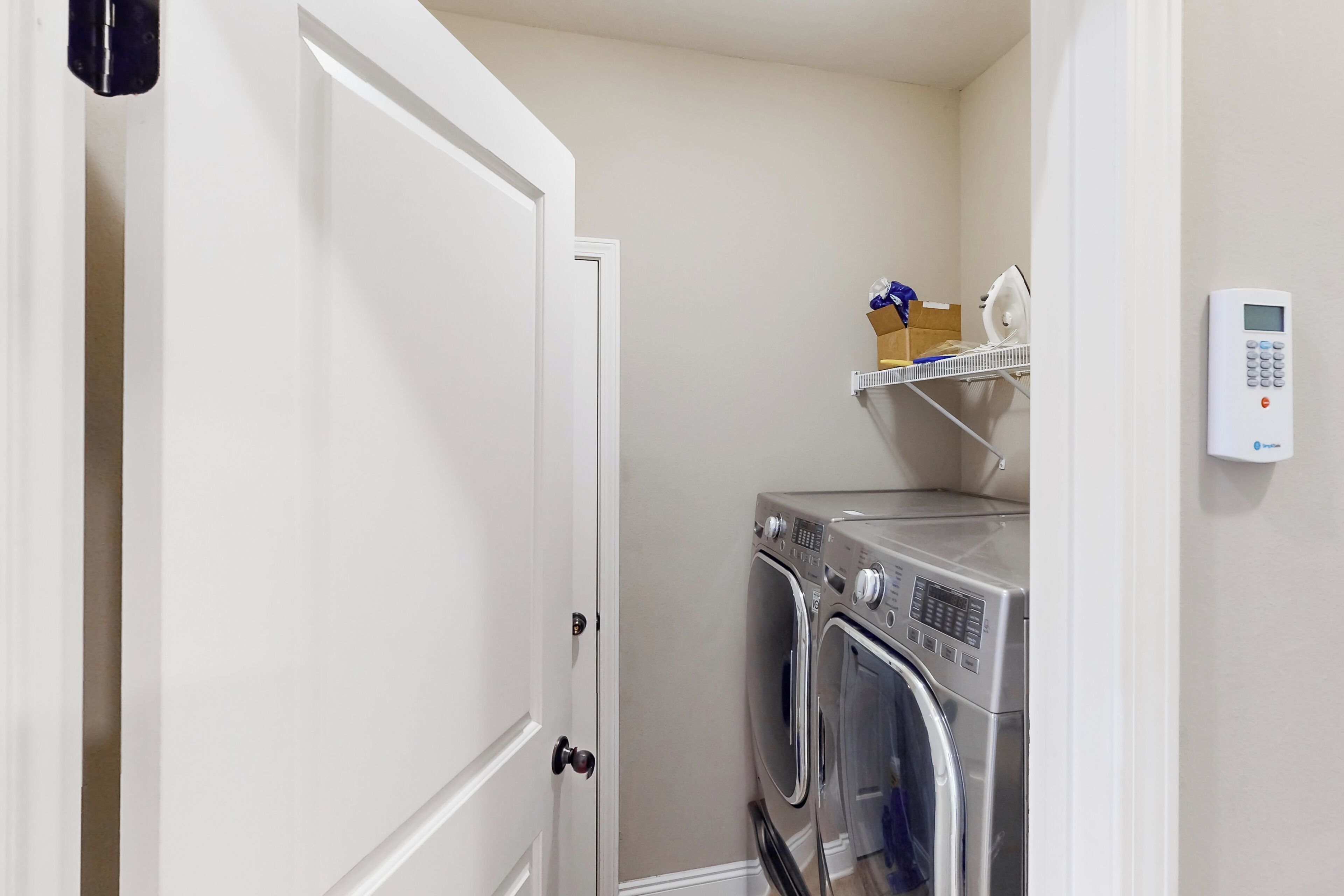 A laundry room with a washing machine and dryer, a shelf with folded clothes, and a digital thermostat on the wall.