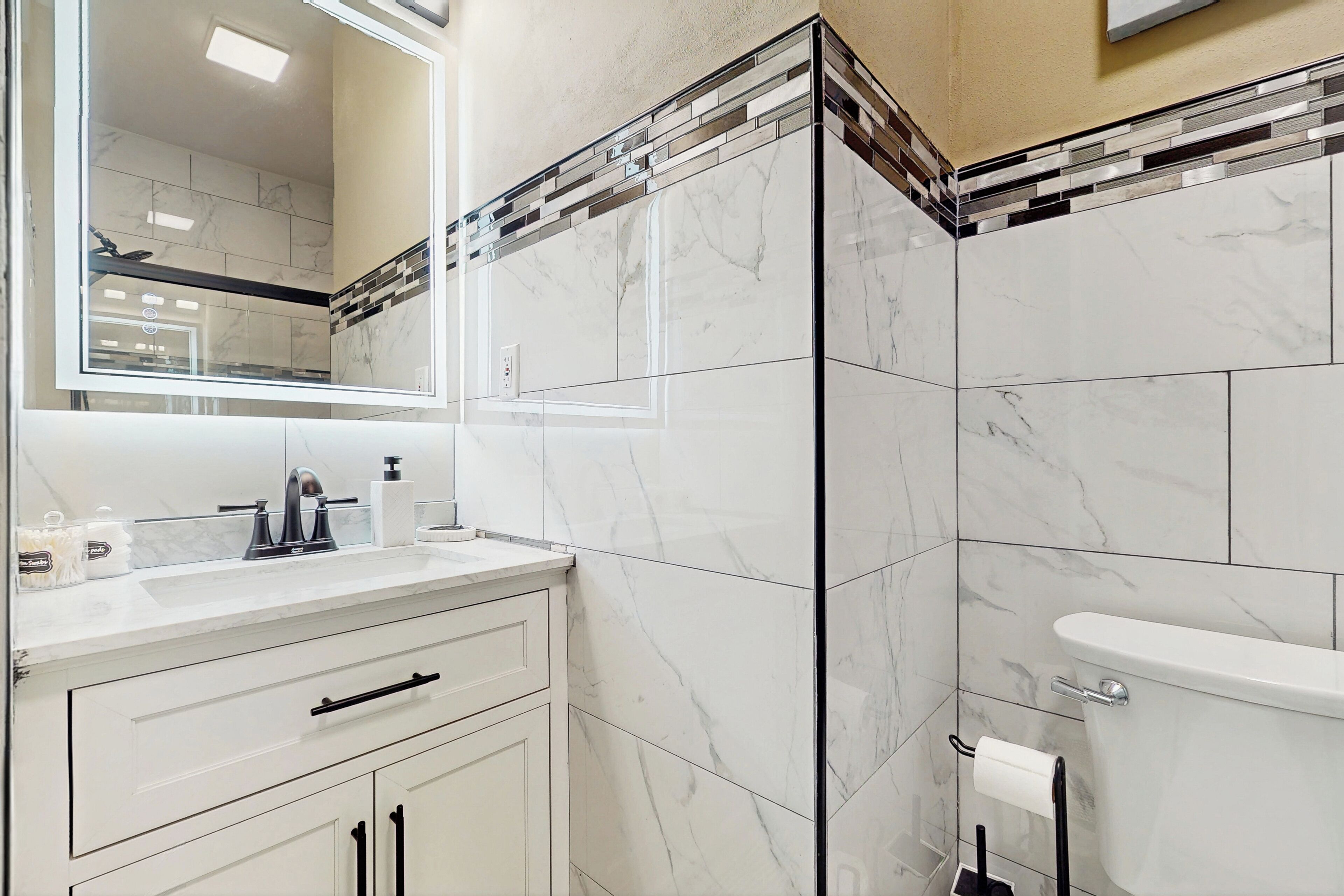 A bathroom with a white vanity, a mirror, a toilet, and a tiled backsplash.
