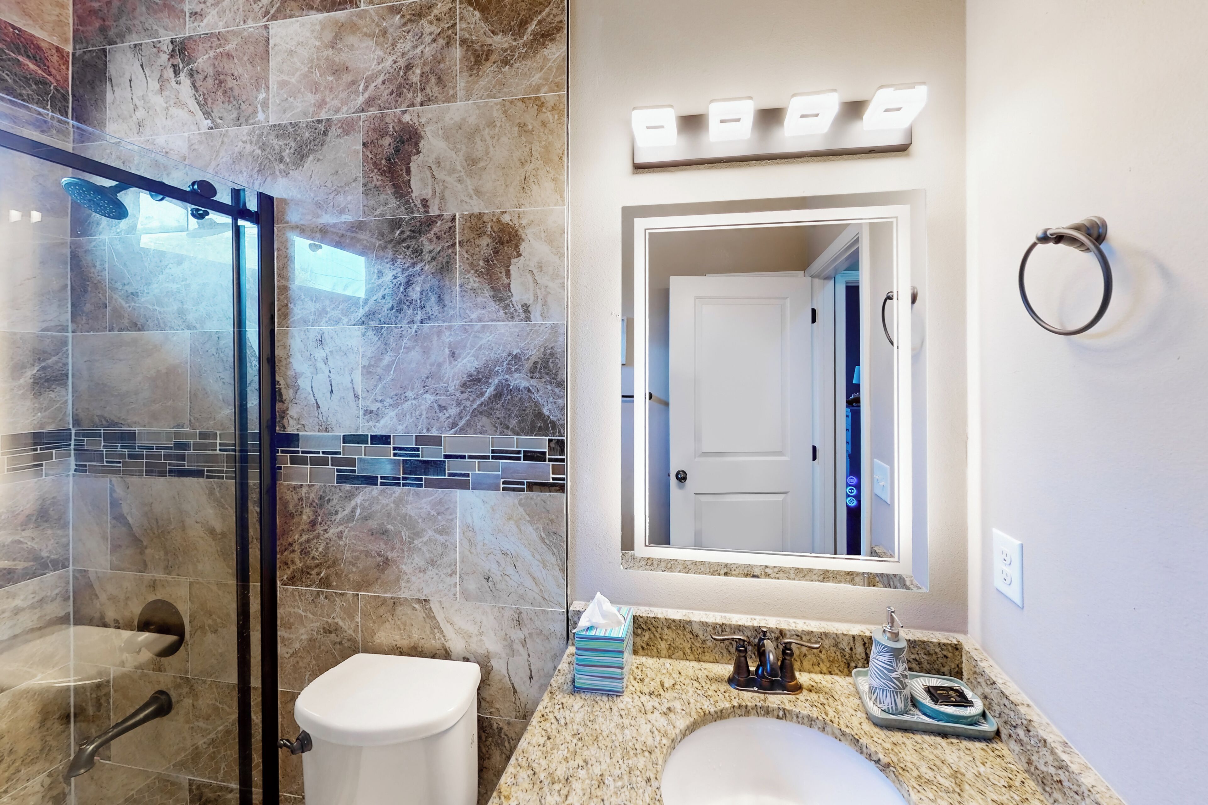 A bathroom with a glass shower enclosure, a toilet, a sink with a marble countertop, and a mirror above the sink.