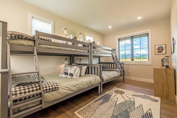 A bunk bed room with a view of mountains through the window, a wooden side table, and a patterned rug. - 3 BR Duplex w/ Full Kitchen, W & D (Driggs)