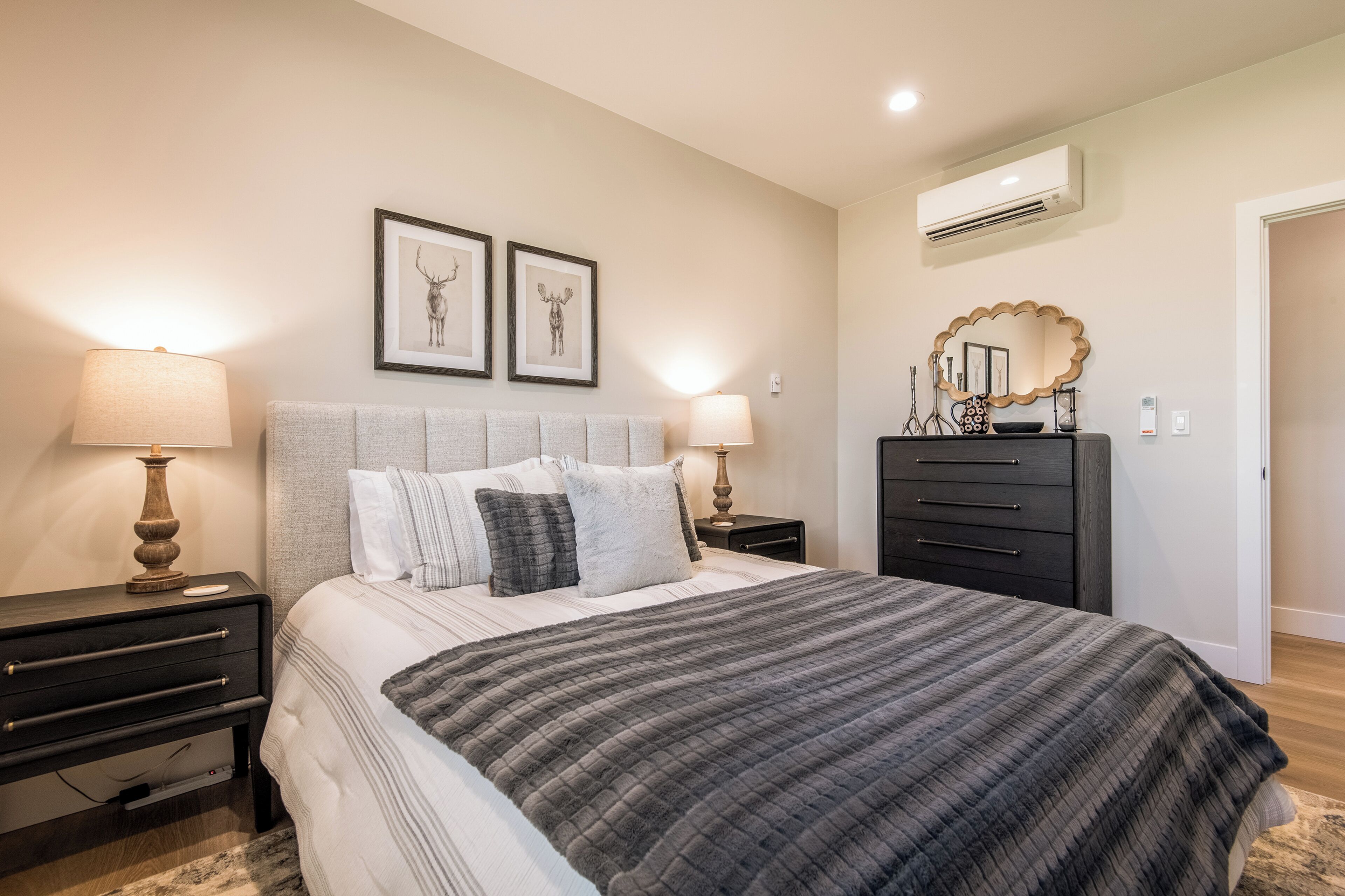 A bedroom with a bed, two bedside tables, a dresser, a mirror, and framed artwork on the wall.
