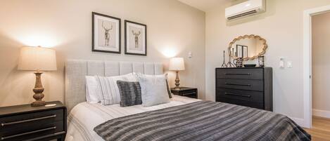 A bedroom with a bed, two bedside tables, a dresser, a mirror, and framed artwork on the wall.