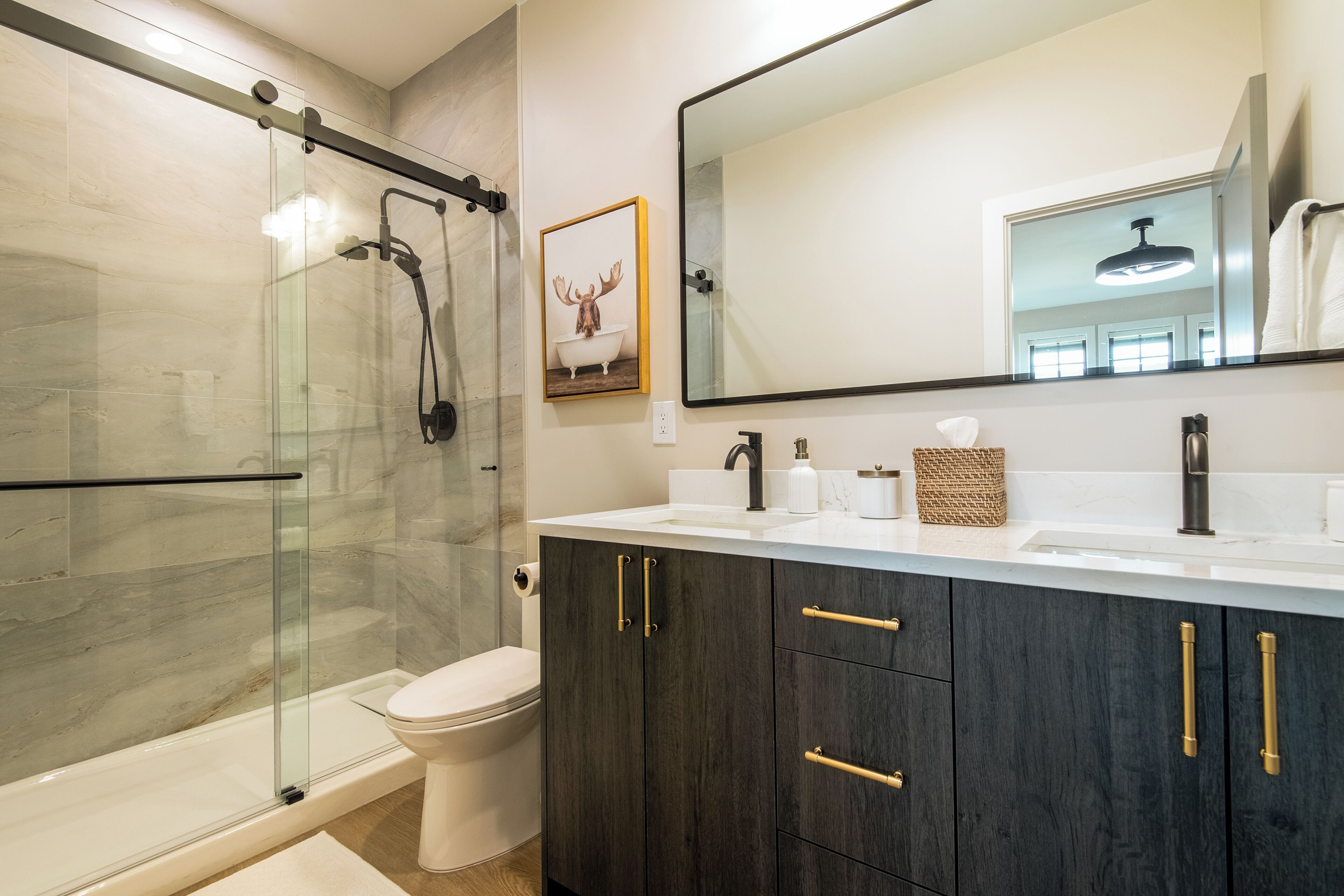 A modern bathroom with a glass-enclosed shower, a toilet, dark wood cabinets, and a large mirror.