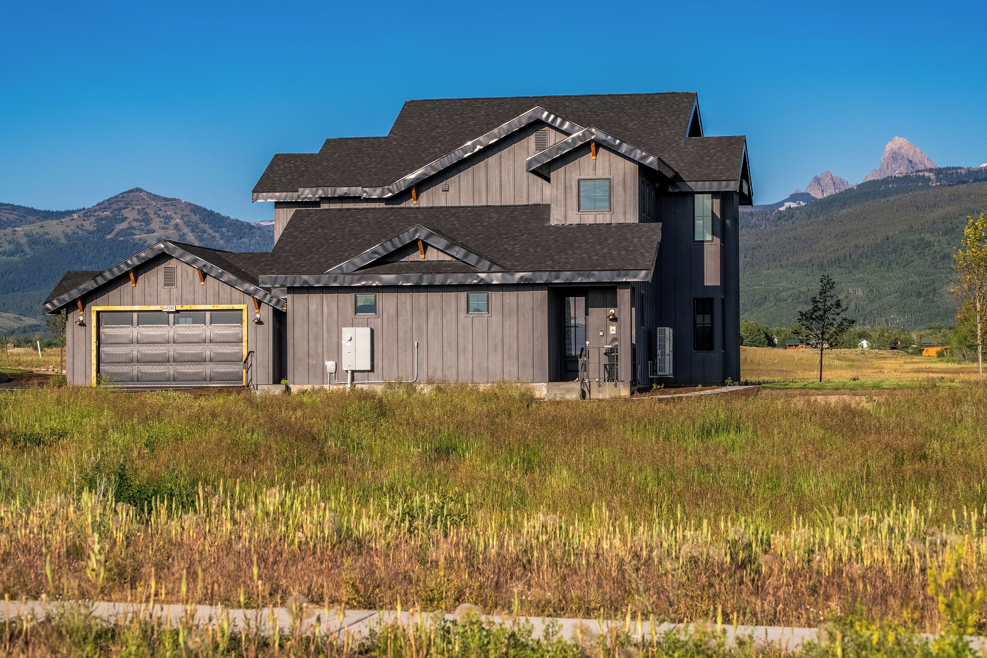 Ein zweistöckiges Haus mit Garage, umgeben von einer Wiese und Bergen im Hintergrund.