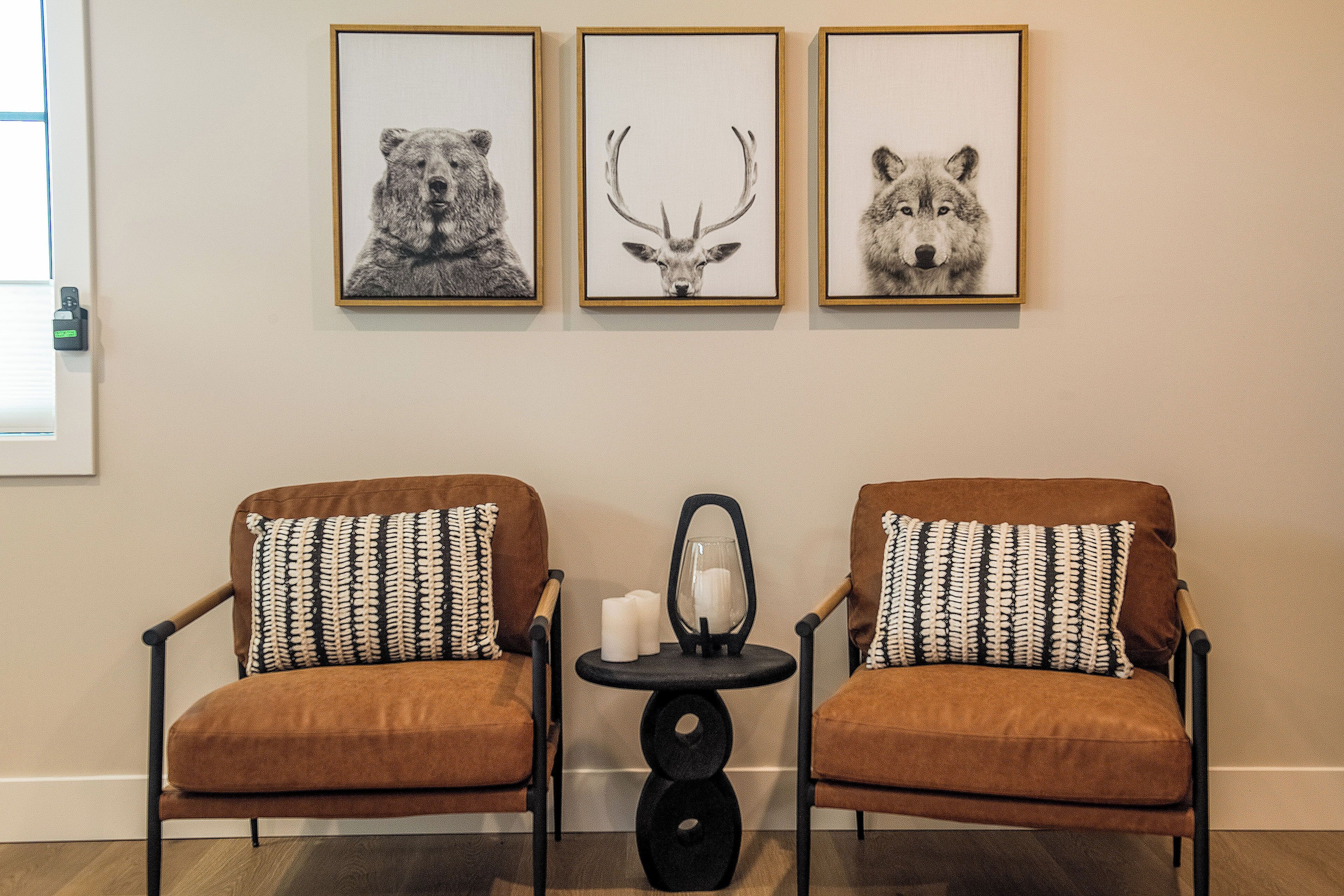 A room with two brown armchairs with patterned cushions, a small round table with candles, and three framed animal prints on the wall.