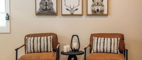 A room with two brown armchairs with patterned cushions, a small round table with candles, and three framed animal prints on the wall.