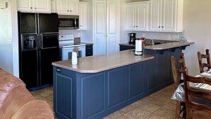 A modern kitchen with white cabinets, a black refrigerator, a built-in oven, a microwave, a coffee maker, and a sink.