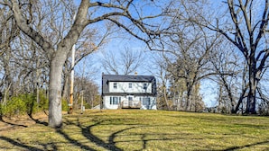 A two-story house with a dark roof and white walls, surrounded by trees and a grassy yard. - Home w/ Spacious Yard, 3 Mi to Dtwn Des Moines! (Des Moines)