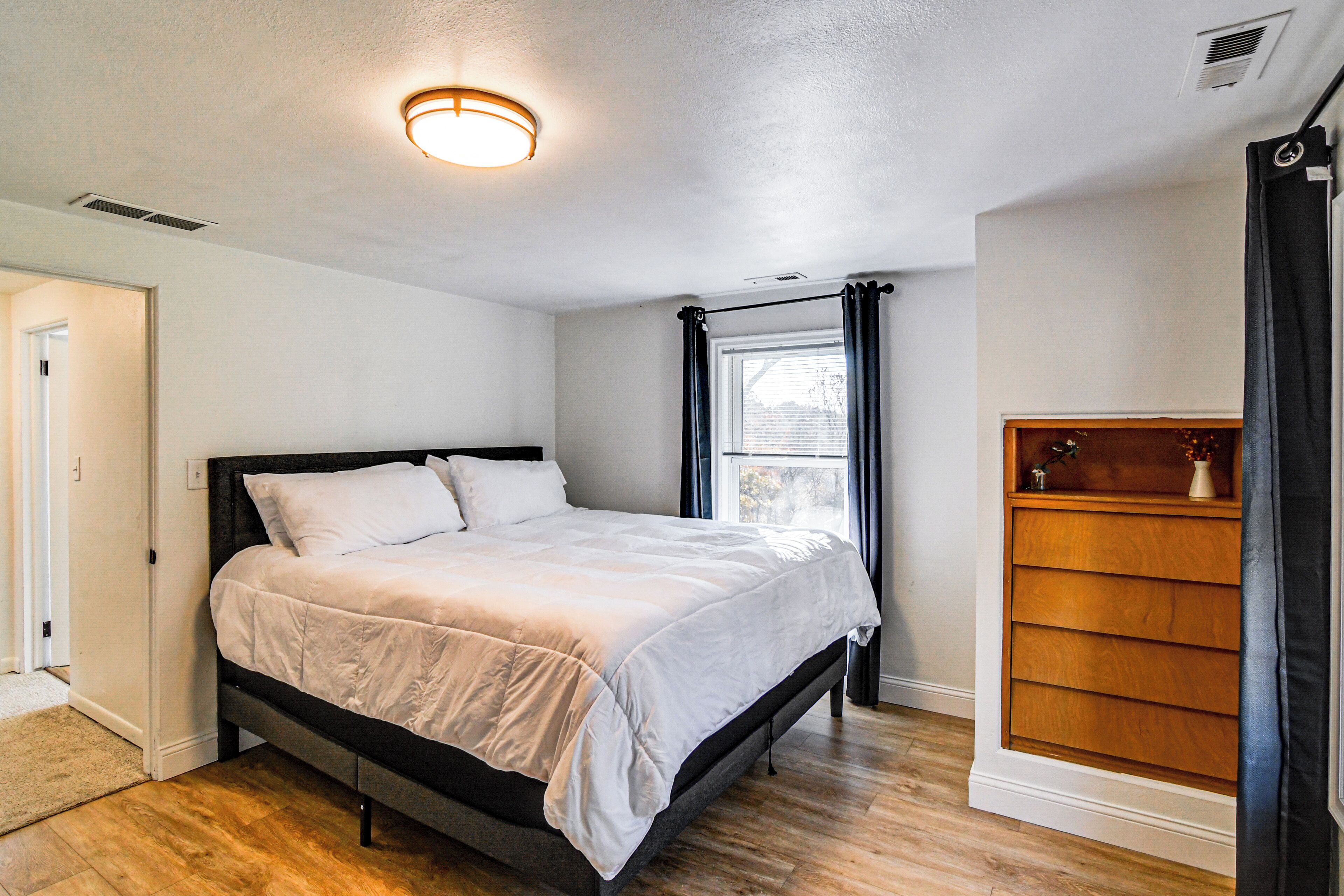 A bedroom with a bed, a wooden dresser, and a window with curtains.
