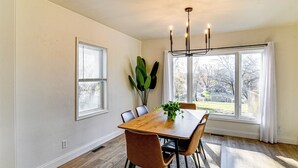 A dining room with a wooden table, six chairs, a chandelier, and large windows with curtains. - Home w/ Spacious Yard, 3 Mi to Dtwn Des Moines! (Des Moines)