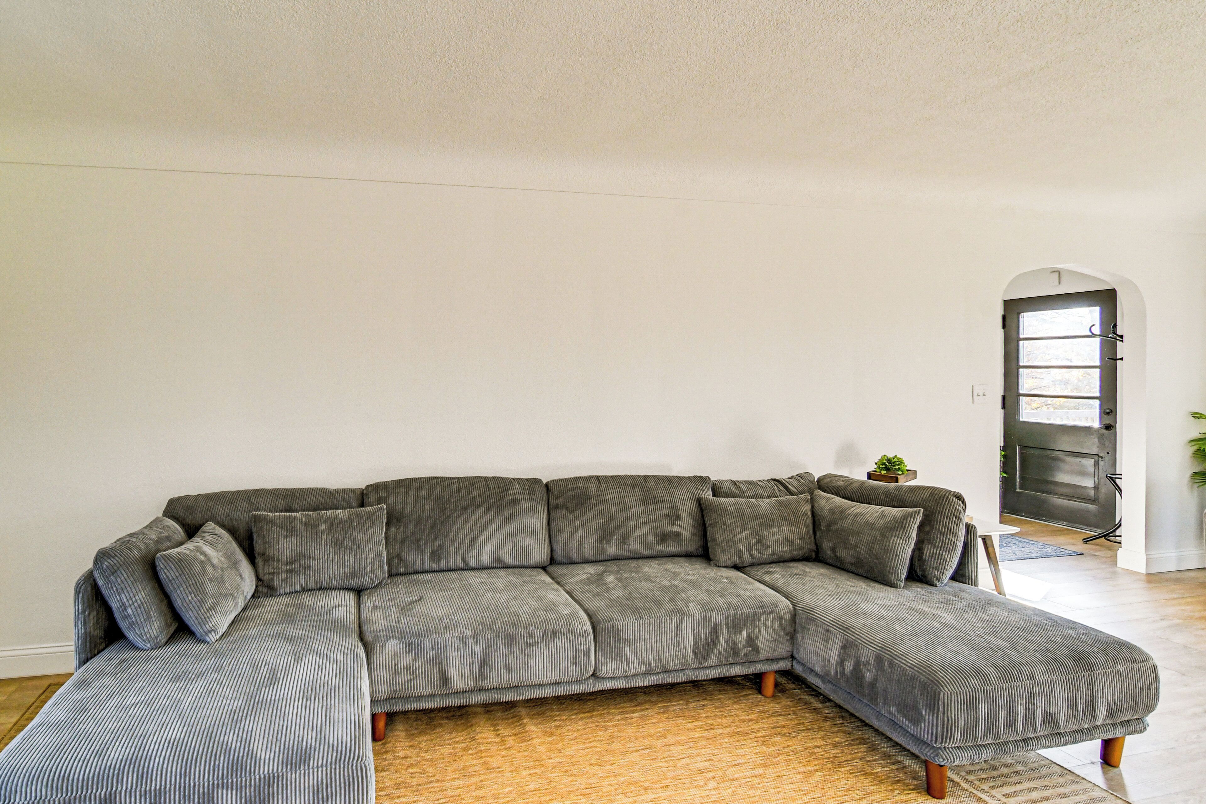 A grey sectional sofa with wooden legs in a room with white walls and a wooden floor.