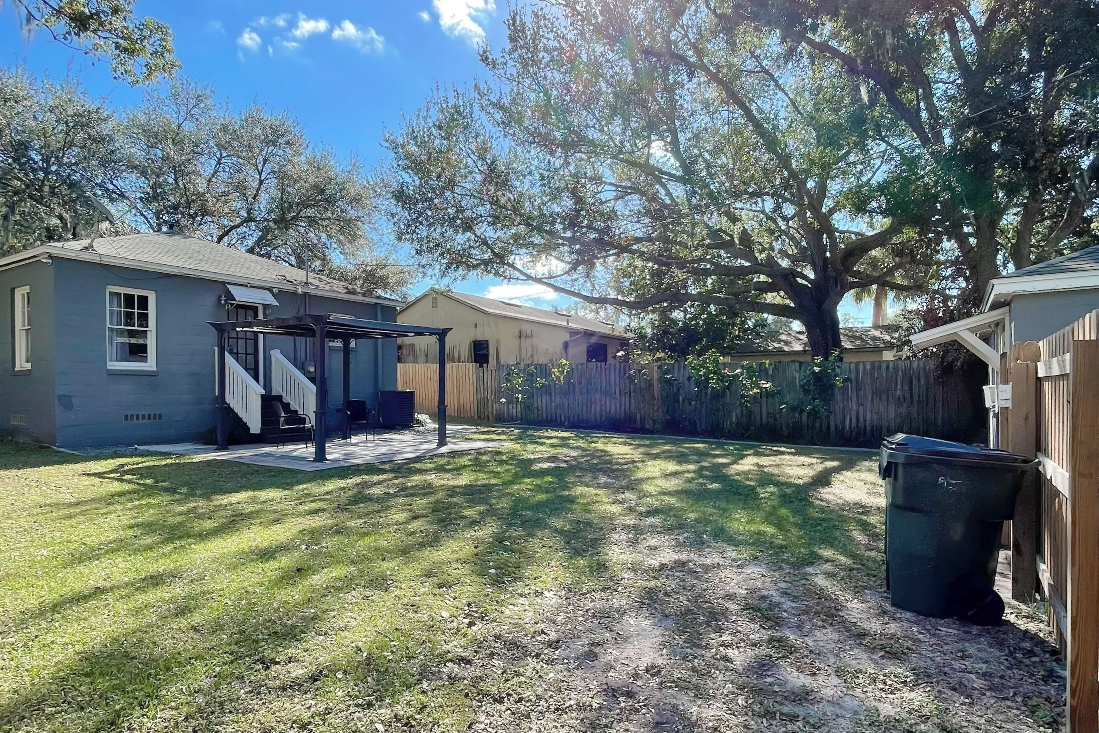 A backyard with a covered patio, a wooden fence, and a large tree providing shade.