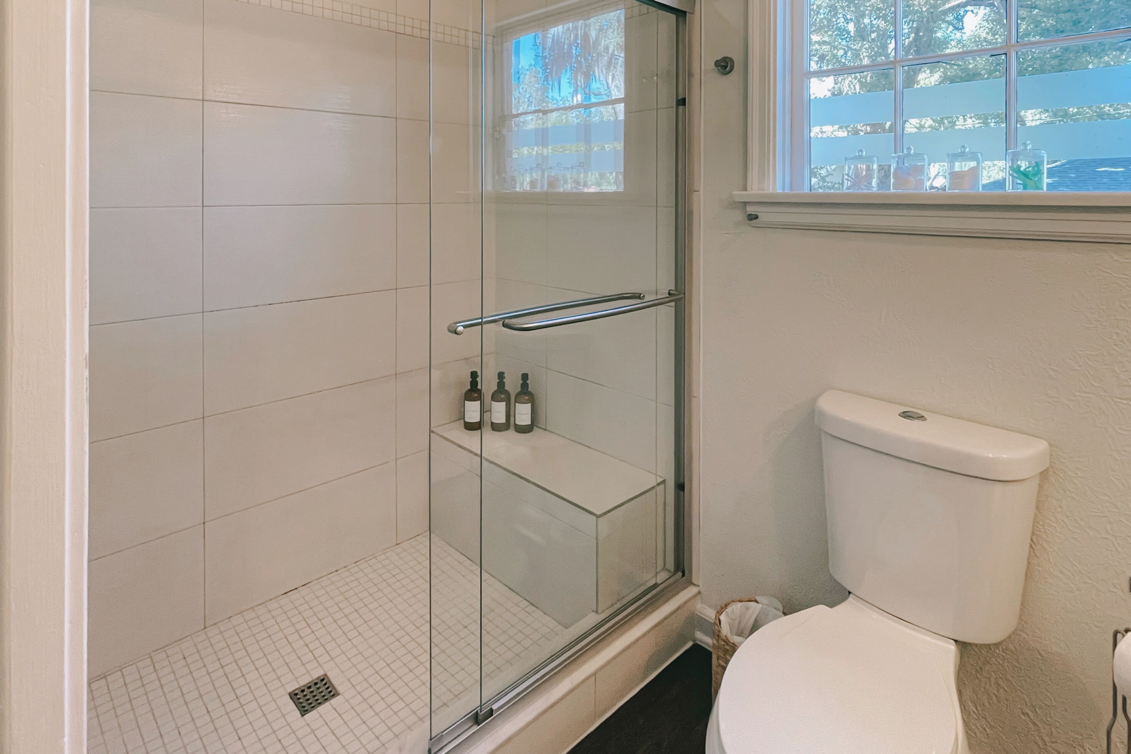 A bathroom with a glass shower enclosure, a toilet, and a window with a view of trees.