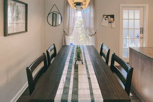 Un comedor con una mesa larga, sillas, un corredor decorativo, un espejo y una puerta con vista al exterior.