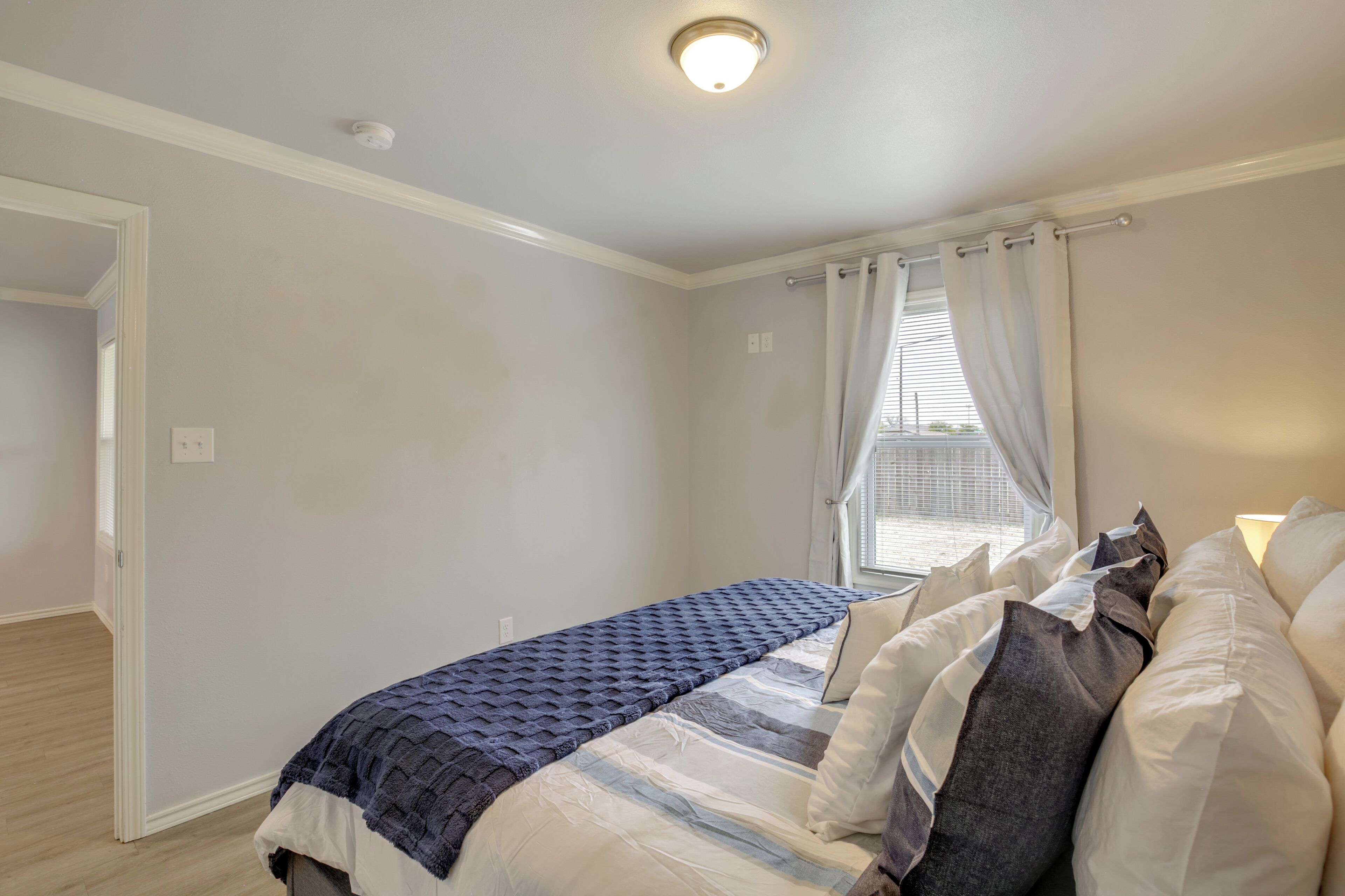 Ein Schlafzimmer mit Bett, einem Fenster mit Vorhängen, einer Tür und einer Deckenleuchte.