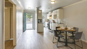 Une cuisine moderne avec des meubles blancs, une table à manger et quatre chaises, et une vue sur l’extérieur.